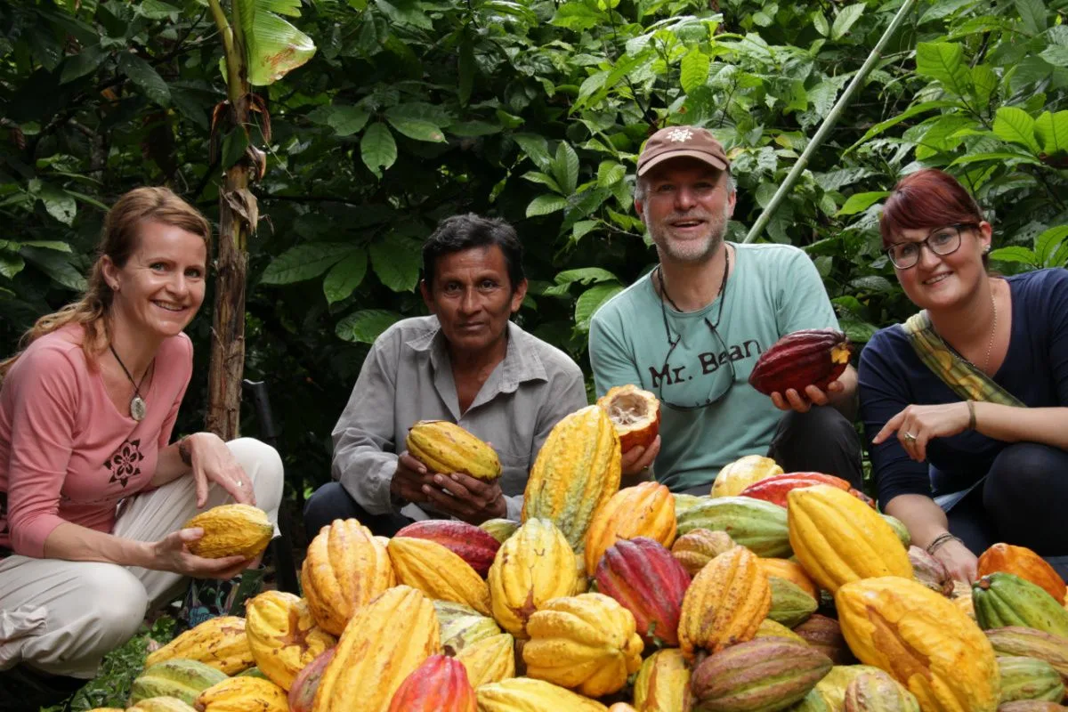 Patrick Walther und Peggy Walther auf einer Plantage mit heimischen. Sie halten frischen Kakao in die Luft.